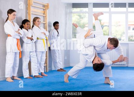 Judo-Trainer zeigt Kampftechniken im Sparring mit einem Jungen für eine Gruppe junger Athleten Stockfoto