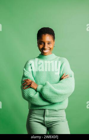 Porträt einer fröhlichen jungen schönen Frau in grünen Kleidern, die vor grünem Hintergrund steht. Eine junge Frau, die in die Kamera schaut. Stockfoto