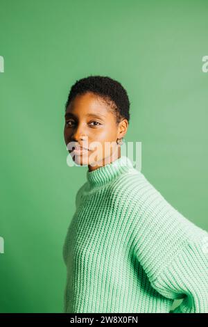 Porträt einer ernsten jungen schönen Frau in grünen Kleidern, die vor grünem Hintergrund steht. Eine junge Frau, die in die Kamera schaut. Stockfoto