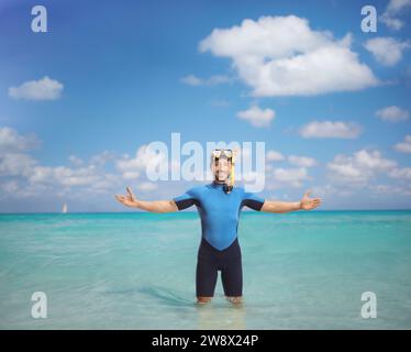 Glücklicher junger Mann, der einen Taucheranzug und eine Maske trägt und ins Wasser steht Stockfoto
