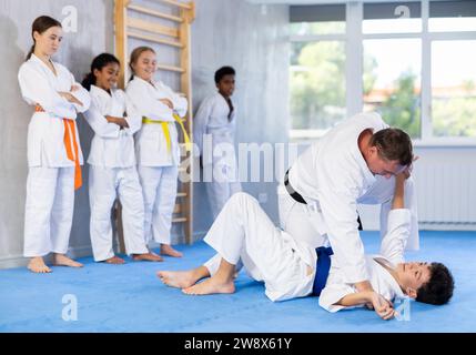 Judo-Trainer zeigt Kampftechniken im Sparring mit einem Jungen für eine Gruppe junger Athleten Stockfoto