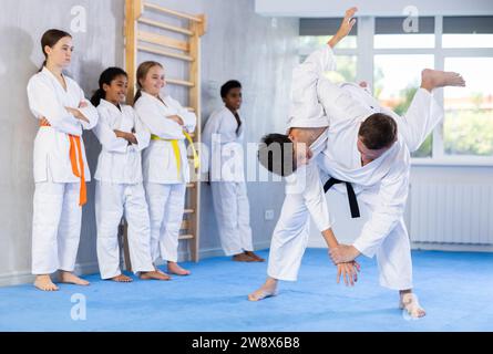 Judo-Trainer zeigt Kampftechniken im Sparring mit einem Jungen für eine Gruppe junger Athleten Stockfoto