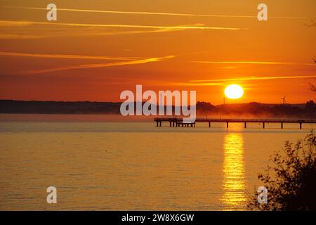 Das Bild zeigt einen Sonnenuntergang in der Ostsee in Deutschland. Der Himmel ist in verschiedenen Orange-Tönen gemalt. Ein Pier erstreckt sich bis ins Meer. Deutschland, Ostsee Stockfoto