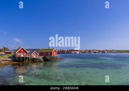 Traditionelle rote norwegische Rorbuer-Hütten stehen auf Stelzen über dem klaren smaragdgrünen Wasser von reine, Lofoten-Inseln Stockfoto