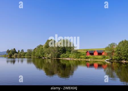 Eine lebhafte Sommerszene in Snasavatnet, Norwegen, mit bezaubernden roten Bootshäusern am Ufer des Sees vor dem Hintergrund des klaren blauen Himmels, Epito Stockfoto