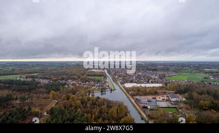 Dieses Luftbild fängt das Wesen einer ländlichen Landschaft unter einem dramatischen bewölkten Himmel ein. Ein sich windender Fluss durchzieht die Szene und spiegelt die Grautöne des Himmels wider. Er wird von Grün und Bäumen umgeben, die auf die wechselnden Jahreszeiten hinweisen. Das nahe gelegene Wohngebiet mit seinen Häusern ist von offenen Feldern durchsetzt, was auf eine Gemeinschaft hindeutet, die in Harmonie mit der umliegenden natürlichen Umgebung lebt. Das Bild weckt eine ruhige und introspektive Stimmung, wobei die Weite von Himmel und Land ein Gefühl von Offenheit und ruhiger Einsamkeit vermittelt. Bedeckter Himmel über einem ländlichen Land Stockfoto