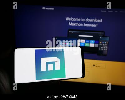 Person, die ein Mobiltelefon mit dem Logo des Webbrowserunternehmens Maxthon vor der Unternehmenswebsite hält. Schwerpunkt auf dem Display des Telefons. Stockfoto
