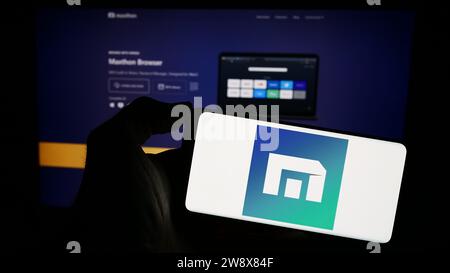 Person, die ein Mobiltelefon mit dem Logo des Webbrowserunternehmens Maxthon vor der Unternehmenswebseite hält. Schwerpunkt auf dem Display des Telefons. Stockfoto
