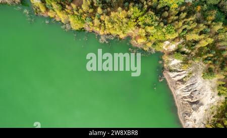 Dieses Bild ist aus der Luftperspektive aufgenommen und erfasst die anmutige Kurve eines Flusses, der sich durch eine üppige Landschaft schlängelt. Das lebhafte grüne Wasser steht in starkem Kontrast zum felsigen Damm auf der einen Seite, wo Erosion Muster sichtbar sind, die die dynamischen Kräfte der Natur im Spiel zeigen. Das gegenüberliegende Ufer ist mit einem Wandteppich von Bäumen in verschiedenen Herbsttönen gesäumt, deren Laub auf die wechselnden Jahreszeiten hindeutet. Die Komposition hebt die Schnittmenge von Wasser, Erde und Leben hervor und zeigt die vielfältigen Texturen und Farben der natürlichen Welt. Blick aus der Vogelperspektive auf eine grüne Flussbiegung mit Roc Stockfoto