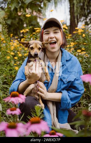 Porträt einer glücklichen jungen Frau mit Terrierhund, der zwischen Blumen im Park kniet Stockfoto