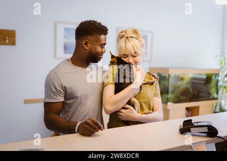 Frau, die Hund vom Mann an der Rezeption in der Tierklinik umschließt Stockfoto