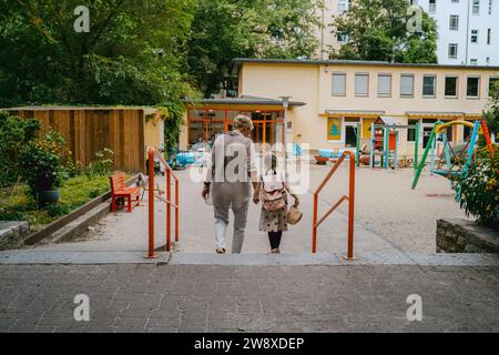 Rückansicht einer Seniorin mit Enkelin, die in Richtung Kindergarten geht Stockfoto