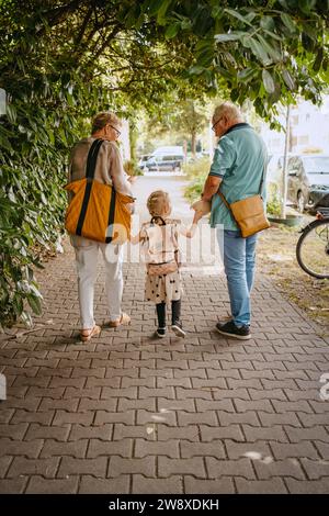 Großeltern halten Hände der Enkelin, während sie auf dem Fußweg laufen Stockfoto