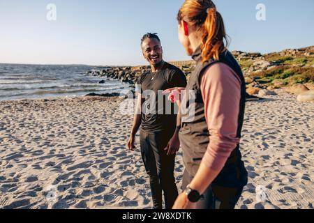 Die Seite der Frau, die mit einem jungen Mann während des Gruppentrainings am Strand auf Sand steht Stockfoto