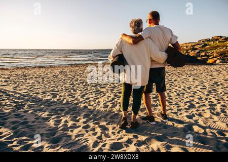 Rückansicht eines Seniorenpaares mit Trainingsmatten, während er am Strand auf Sand steht Stockfoto