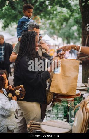 Lächelnde Frau mit Papiertüte beim Einkaufen mit der Familie auf dem Flohmarkt Stockfoto