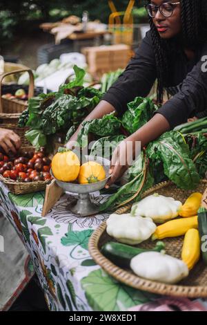 Hochwinkelansicht der weiblichen Verkäuferin, die gelbe Zucchini auf dem Bauernmarkt hält Stockfoto