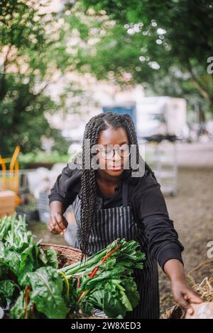 Weibliche Gemüseverkäuferin, die in der Nähe des Verkaufsstandes auf dem Bauernmarkt arbeitet Stockfoto