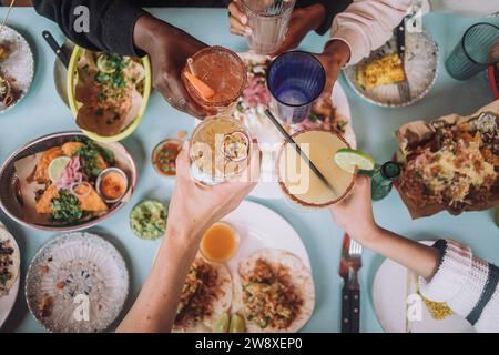 Direkt über dem Blick auf Hände, die ein Glas frischer Cocktails beim Feiern im Restaurant toasten Stockfoto