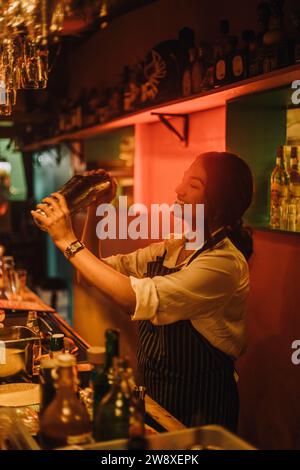 Lächelnde Barkeeperin bereitet Cocktails zu, während sie an der Bar arbeitet Stockfoto