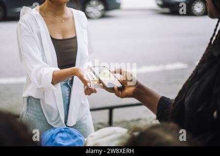 Frau, die beim Einkaufen auf dem Flohmarkt Online-Zahlungen über mobile App tätigt Stockfoto