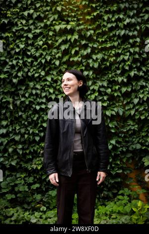 Lächelnde junge Frau, die wegschaut, während sie vor der Hecke im Park steht Stockfoto