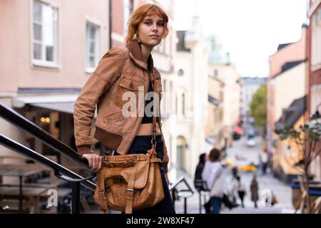 Porträt einer jungen Frau mit Tasche und Jacke, die in der Stadt am Geländer stand Stockfoto