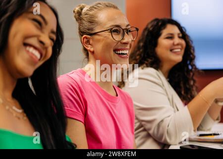 Glückliche Geschäftsfrauen lachen mit weiblichen Kollegen während des Treffens im Büro Stockfoto