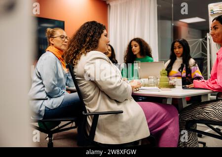 Seitenansicht einer Unternehmerin, die mit Kollegen während eines Geschäftstreffens im Büro sitzt Stockfoto