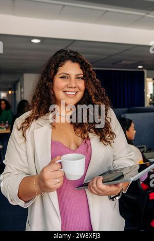 Porträt einer lächelnden jungen Geschäftsfrau, die im Büro eine Kaffeetasse hält Stockfoto