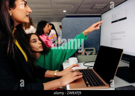 Geschäftsfrau, die auf den Bildschirm zeigt, und Kollege, der im Büro am Laptop arbeitet Stockfoto
