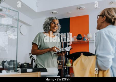 Senior weibliche Unternehmerin mit Kreditkartenleser, die am Checkout-Schalter mit dem Kunden spricht Stockfoto