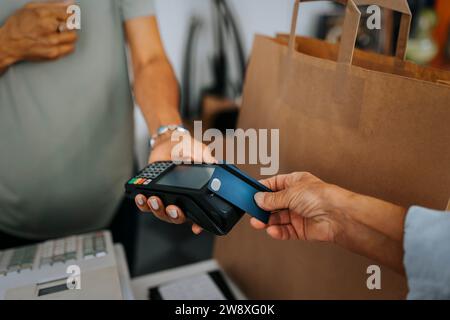 Zugeschnittenes Bild einer Kundin, die beim Auschecken eines Antiquitätengeschäfts mit Kreditkarte an eine Verkäuferin zahlt Stockfoto