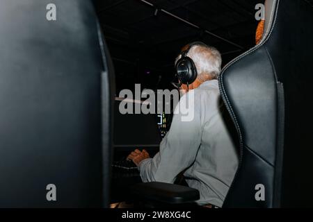 Rückansicht eines älteren Mannes, der am Computer spielt, während er auf einem Stuhl in der Spiellounge sitzt Stockfoto