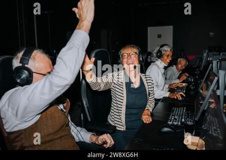 Glückliches Seniorenpaar, das High-Five von männlichen und weiblichen Freunden gibt, während es ein Videospiel in der Spielelounge gewinnt Stockfoto