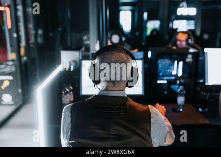 Rückansicht eines älteren Mannes, der während des Wochenendes im Spielezentrum Videospiele spielt Stockfoto
