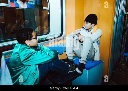 Männliche Freunde, die miteinander reden, während sie in der Straßenbahn sitzen Stockfoto