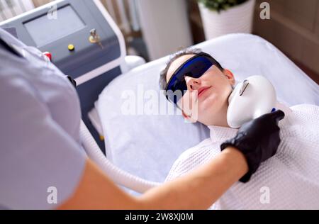 Porträt einer entspannten jungen Klientin, die eine SMAS Ultraschall-Gesichtsliftmassage mit professioneller Ausstattung im Beauty Center erhält Stockfoto