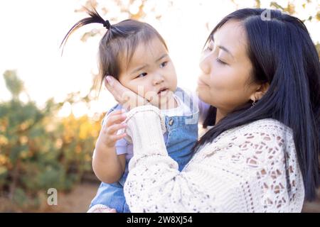 Eine junge Asiatin umarmt ihre kleine Tochter. Eine attraktive Mutter läuft mit ihrem süßen Mädchen draußen. Glückliche koreanische Familie im Park. Stockfoto