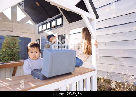 Drei kleine Kinder spielen in einem hölzernen Kinderhaus. Süße asiatische und kaukasische Kinder haben Spaß im Garten. Lächelnder Junge und Mädchen Stockfoto