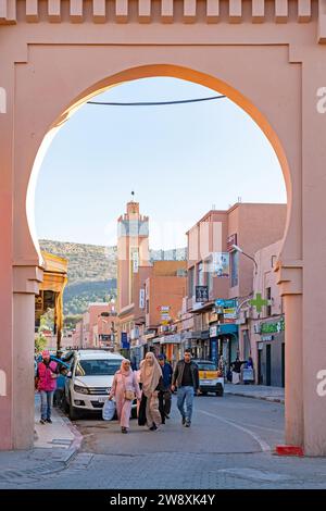 Minarett und Marokkaner, die unter dem pinkfarbenen Stadttor in der Stadt Beni Mellal, Region Béni Mellal-Khénifra, Marokko spazieren Stockfoto