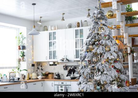 Weihnachtliche Einrichtung in weißer Küche, modernes Innenleben im Dorf mit einem schneebedeckten Weihnachtsbaum und Feenlichtern. Neujahr, Weihnachtsstimmung, gemütliches Zuhause, M Stockfoto