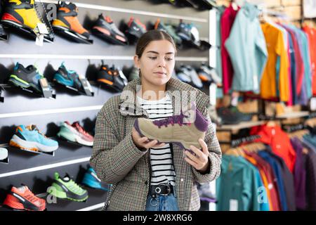 Das junge Mädchen wählt und kauft Winterschuhe für Wanderungen im Sportgeschäft Stockfoto