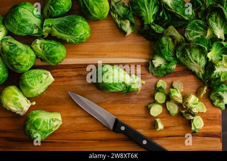 Geschnittene Rosenkohl auf einem Holzschneidebrett: Geschälte und zugeschnittene Babykohl mit Blättern und Stielen auf einem Holzschneidebrett Stockfoto