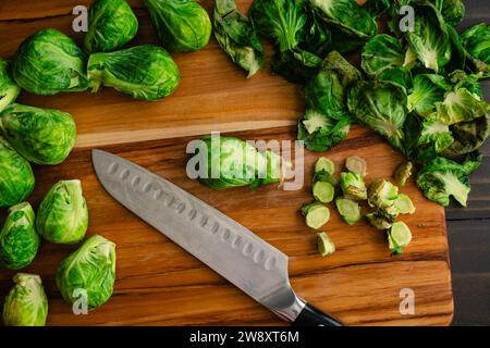 Geschnittene Rosenkohl auf einem Holzschneidebrett: Geschälte und zugeschnittene Babykohl mit Blättern und Stielen auf einem Holzschneidebrett Stockfoto