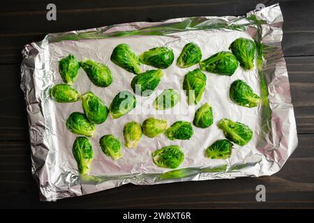 Rohe, halbierte Rosenkohl auf einer mit Folie gefütterten Pfanne: Halbierte Babykohl in Olivenöl gewürzt und mit Salz und Pfeffer gewürzt Stockfoto