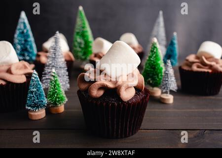 Heiße Kakao-Cupcakes mit Riesenmarshmallows: Schokoladen-Cupcakes mit heißer Schokolade, umgeben von Miniatur-Weihnachtsbaumschmuck Stockfoto