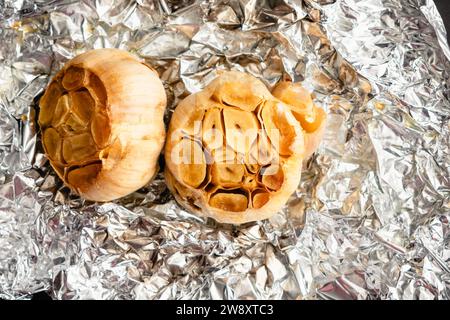 Geröstete Knoblauchköpfe auf zerknitterter Aluminiumfolie: Gebratene Knoblauchzwiebeln, mit nativem Olivenöl extra und Meersalz auf Alufolie getränkt Stockfoto