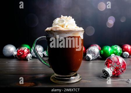 Gewürzter Weihnachtskaffee mit Schlagsahne: Großer Glasbecher mit frisch gebrühtem Gewürzkaffee, umgeben von Weihnachtsschmuck Stockfoto