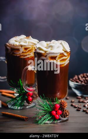 Gewürzter Weihnachtskaffee mit Schlagsahne: Zwei Glasbecher frisch gebrühten Gewürzkaffee mit Weihnachtsdekoration und Zutaten Stockfoto